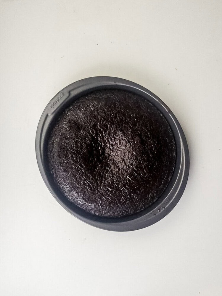 A round, baked chocolate cake in a circular metal pan is shown on a plain white surface.