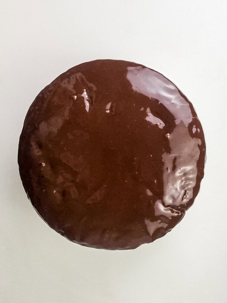 A round dessert covered in smooth, glossy chocolate glaze, photographed from above on a plain white background.