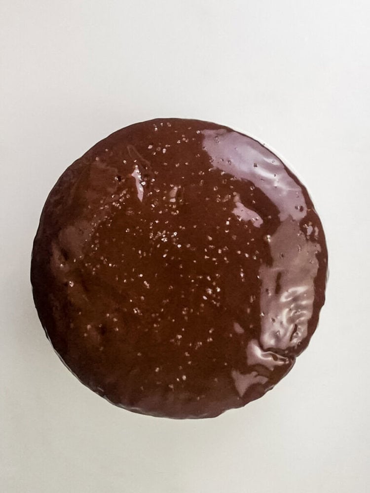A round chocolate-glazed cake is pictured from above on a plain white surface.