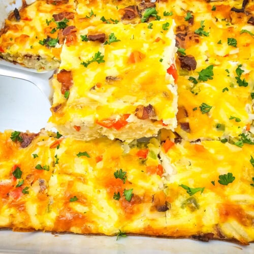 A baked casserole dish with visible cheese, vegetables, and herbs, with a piece being served using a spatula.
