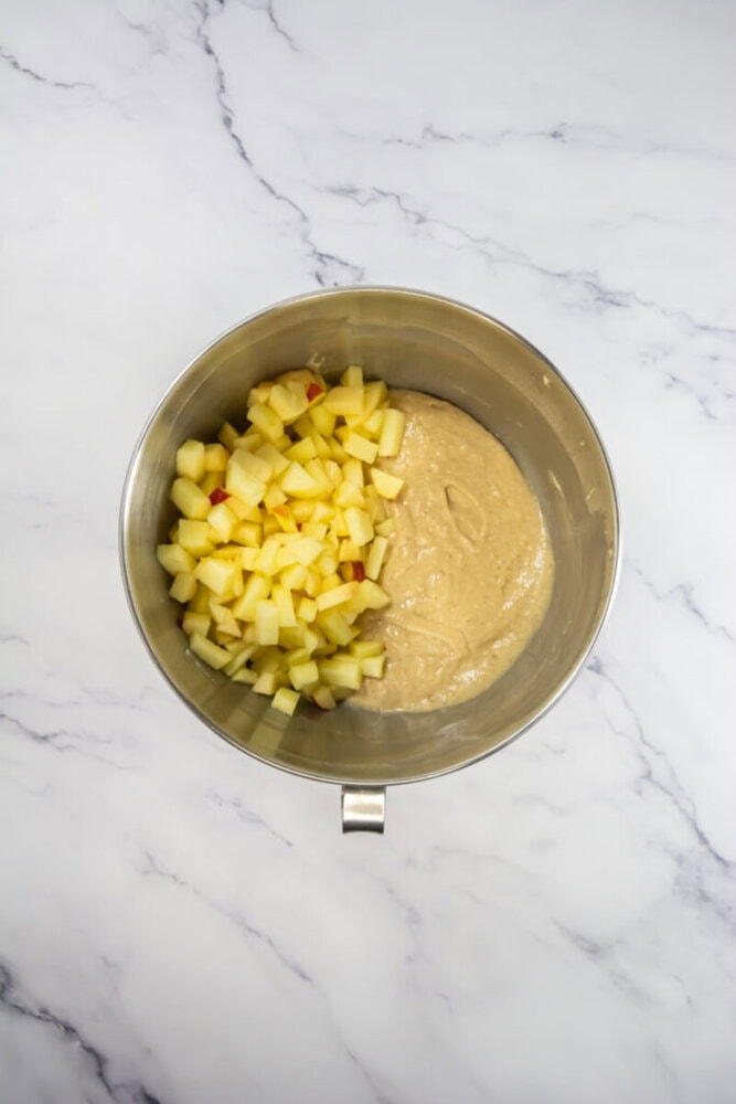 Mixing bowl with chopped apples and batter on a marble surface.