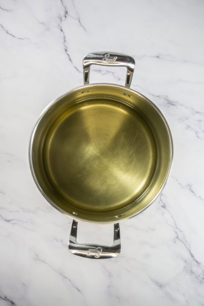 A metal pot filled with oil sits on a marble surface, viewed from above.