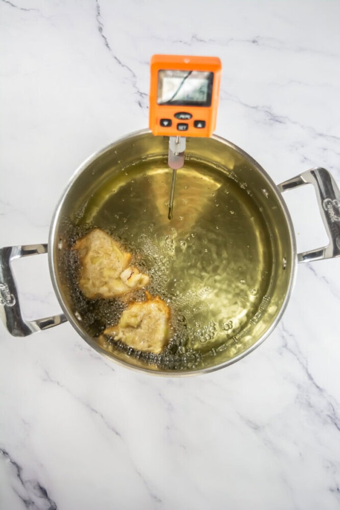 Pot of oil with two pieces of food frying, monitored by an orange digital thermometer.
