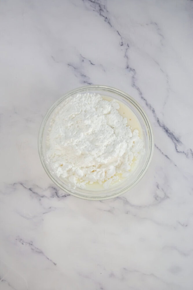 A glass bowl filled with flour on a marble surface.
