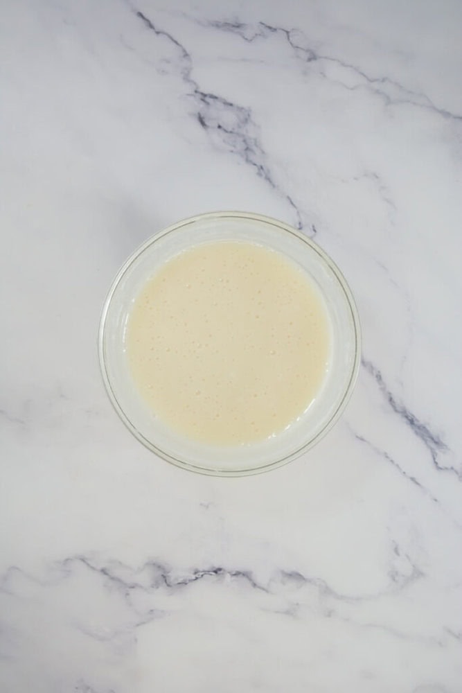 A clear glass bowl filled with a creamy batter on a white marble surface.