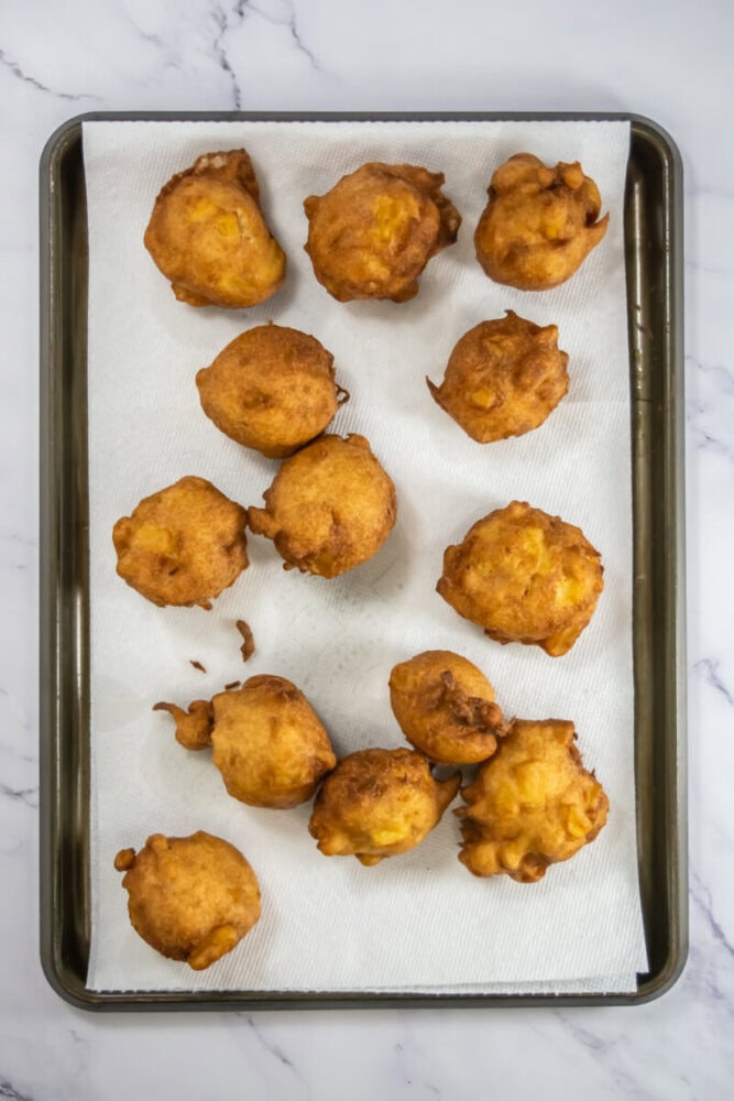 Golden brown fritters on a paper towel-lined baking tray, resting on a marble surface.