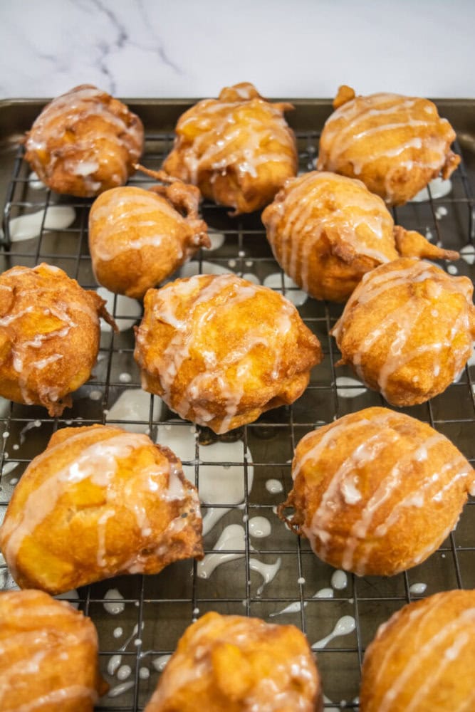 Golden brown fritters drizzled with glaze on a cooling rack over a baking sheet.