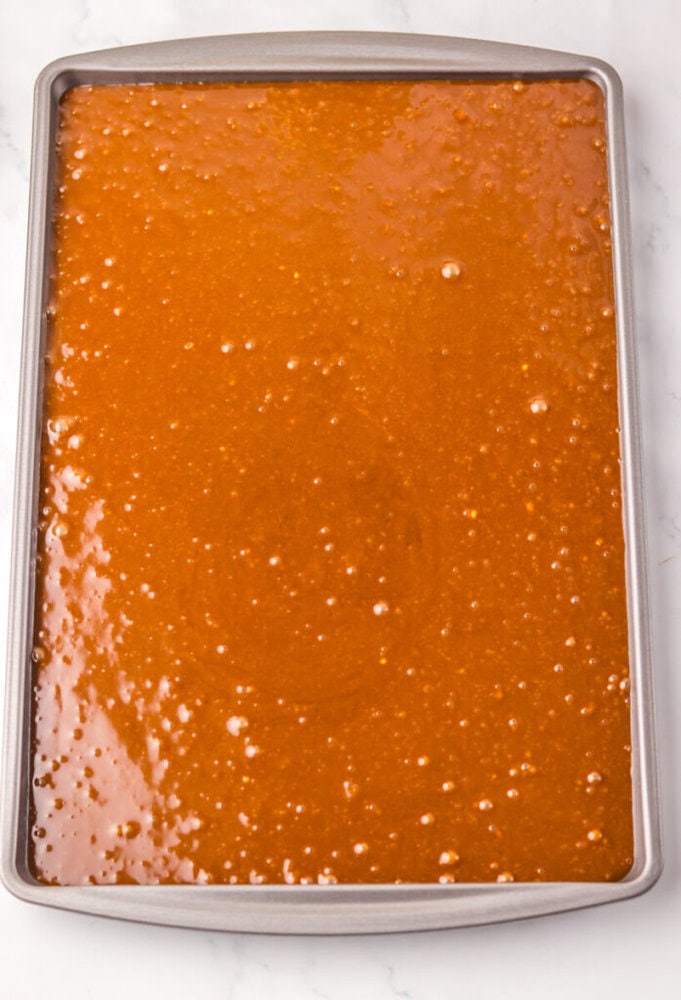 A rectangular baking sheet filled with an even layer of unbaked chocolate cake batter on a white surface.