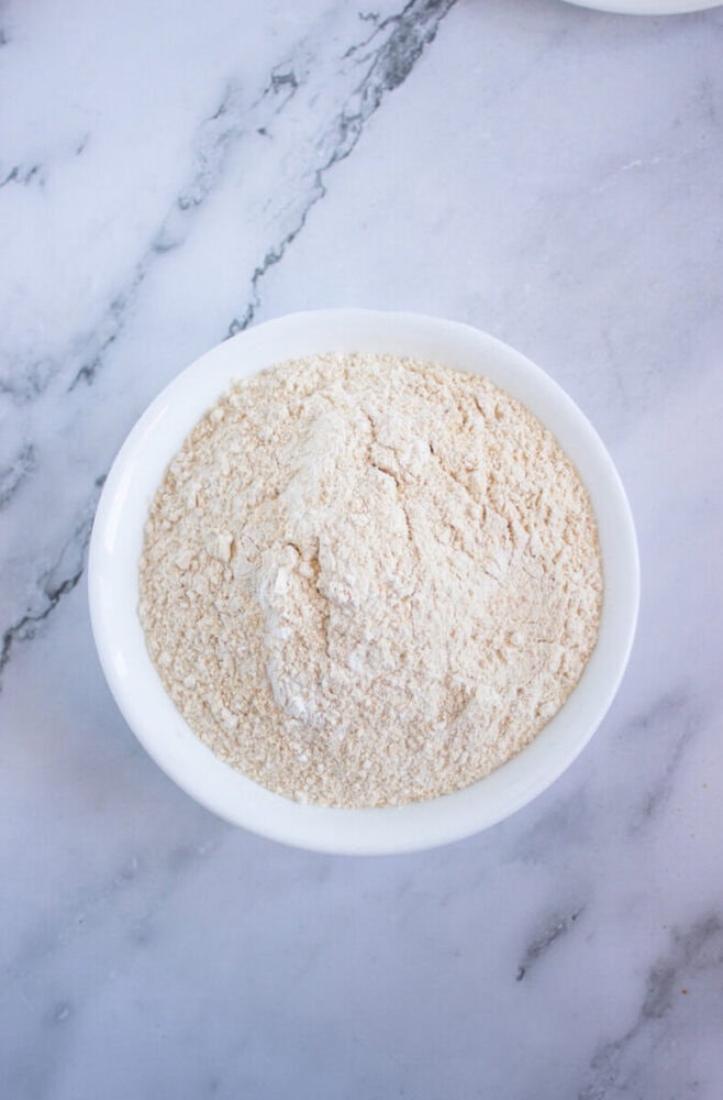 A white bowl filled with flour on a light marble surface.
