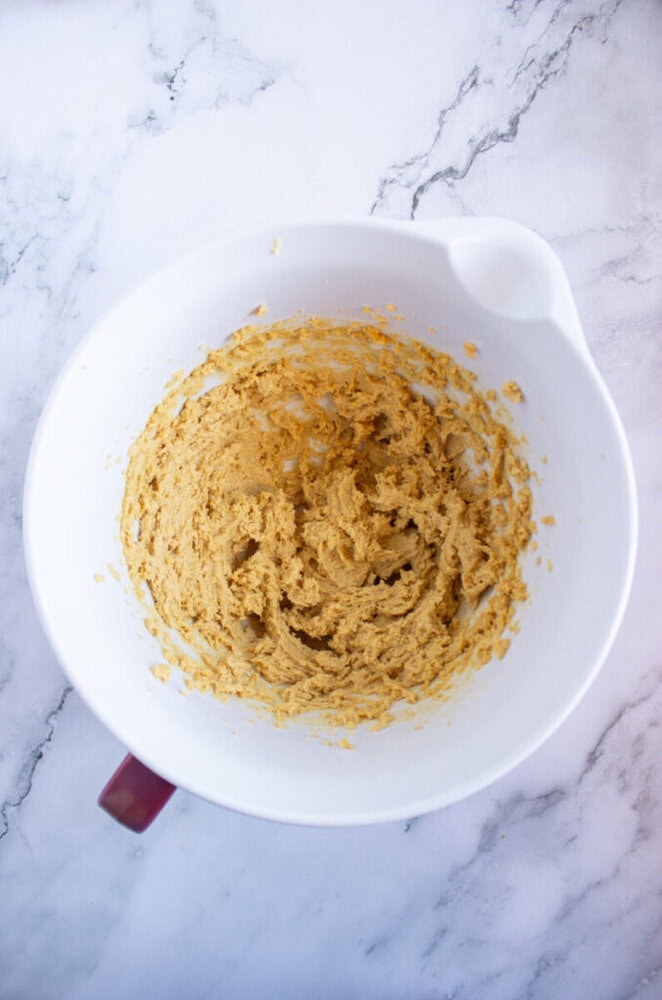 Mixing bowl with thick, beige dough against a marble background.