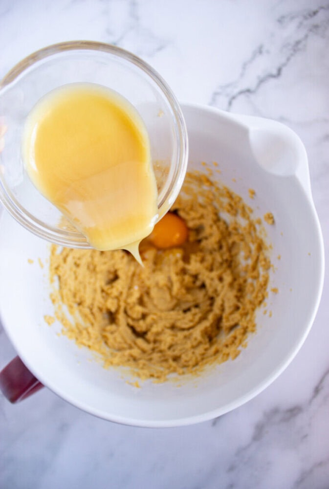 Egg and vanilla mixture being poured into a mixing bowl with creamed butter and sugar.