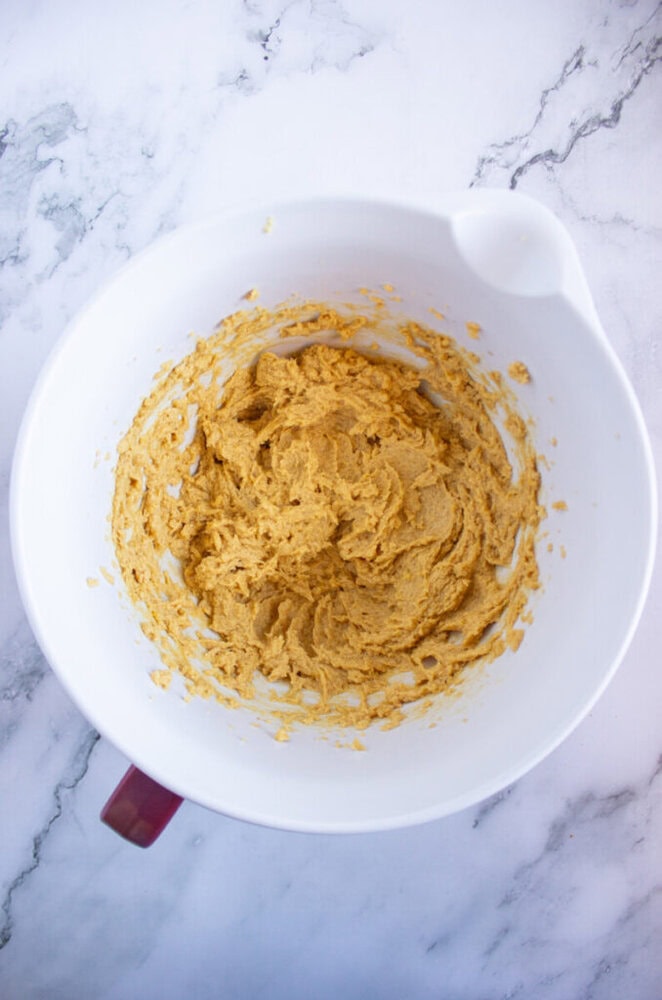 Mixing bowl with creamy, light brown dough on a marble surface.