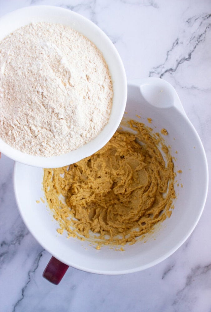 Mixing flour into a bowl of cookie dough on a marble countertop.