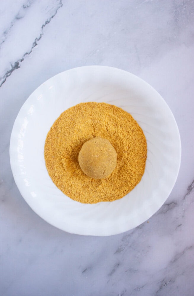 A round ball is placed in a pile of yellow, crumbly powder in a white bowl on a marble surface.