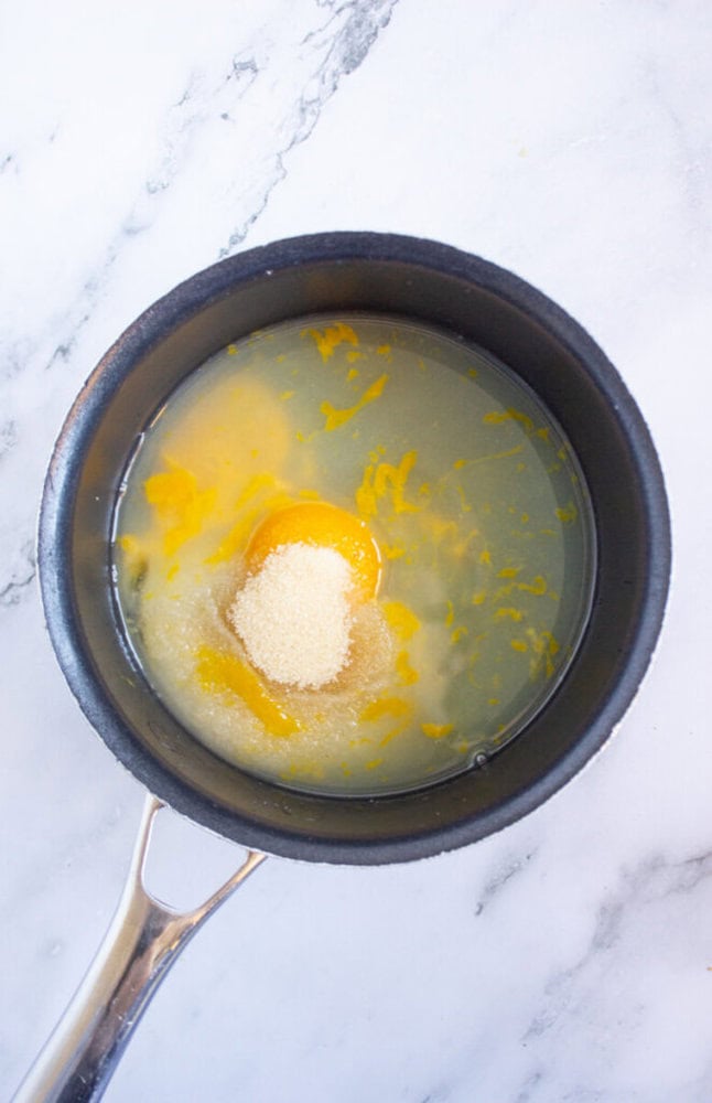 Egg yolks, sugar, and liquid in a small black saucepan on a marble surface.