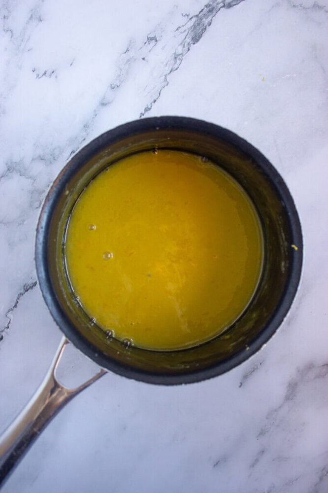 A small saucepan containing a yellow liquid is resting on a marbled surface.