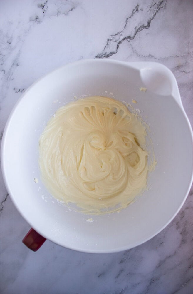 A large white mixing bowl with creamy, whipped batter against a marble countertop.
