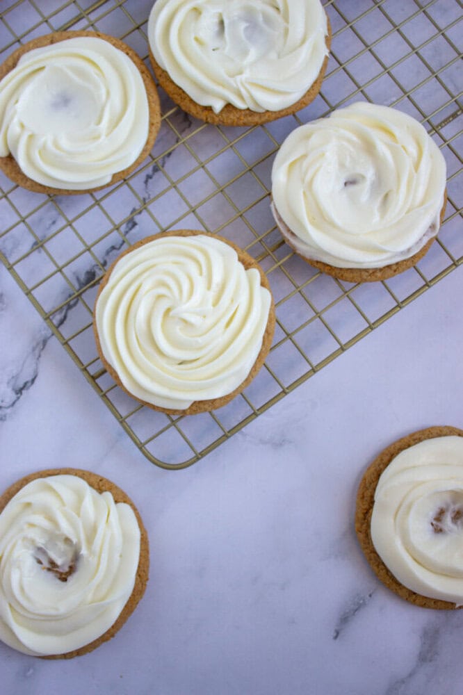 Six cookies with white swirled icing on a cooling rack and marble surface.