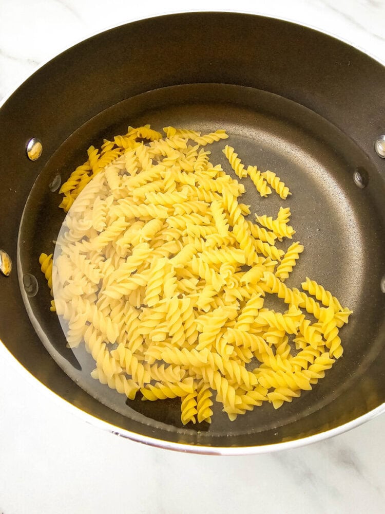 Dry rotini pasta in a pot of water on a stove, ready to be boiled.
