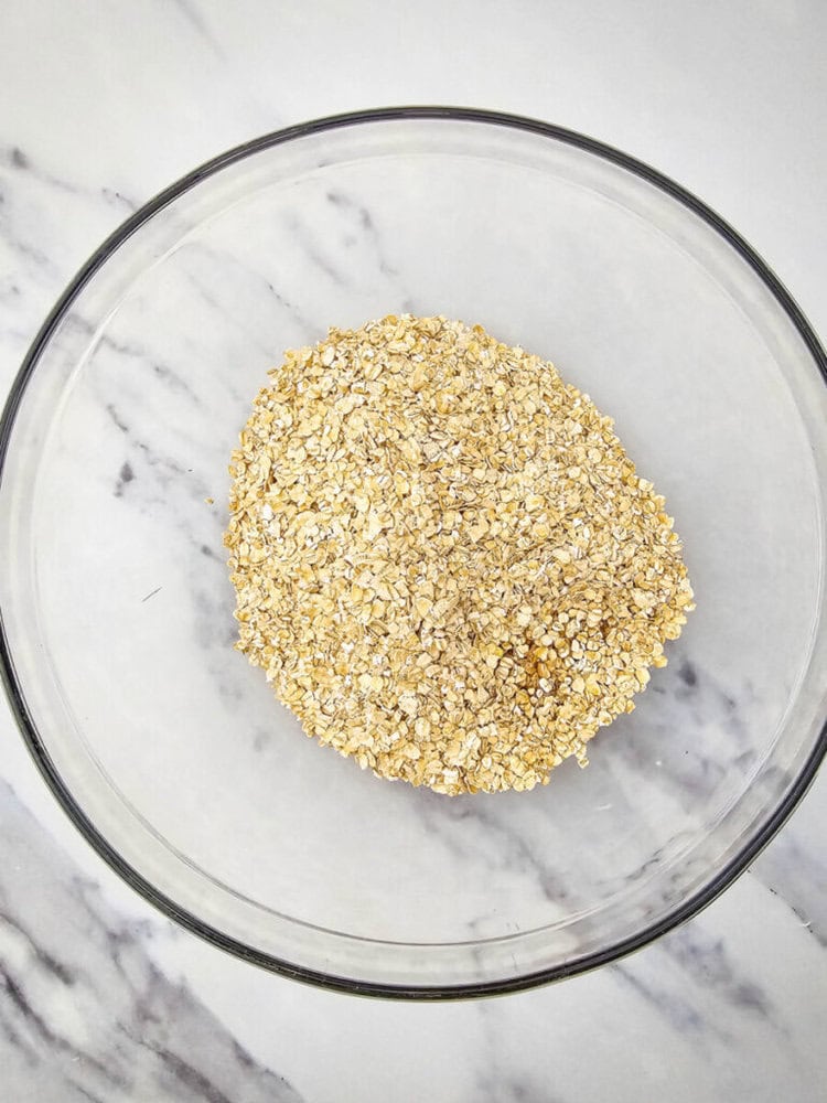 A glass bowl filled with dry oats on a marble countertop.