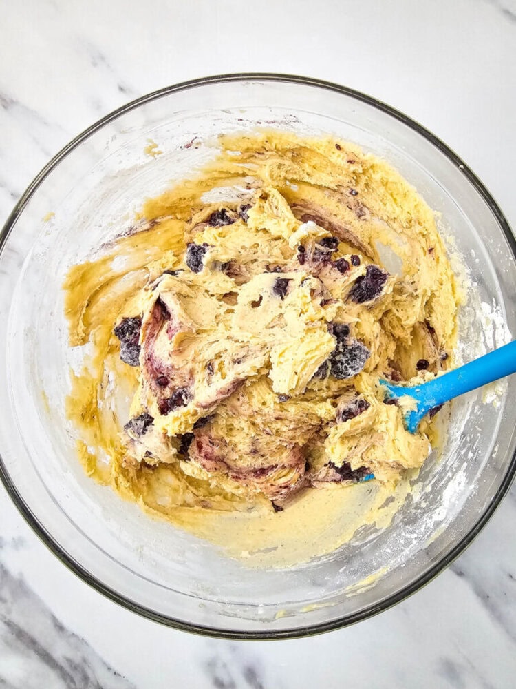 Bowl of mixed cookie dough with chocolate chips and swirls, and a blue spatula on a marble countertop.