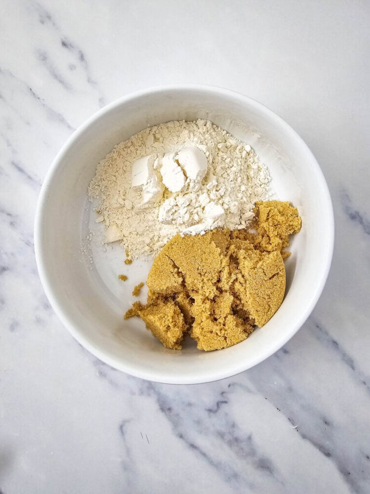 A white bowl containing flour and brown sugar on a marble surface.