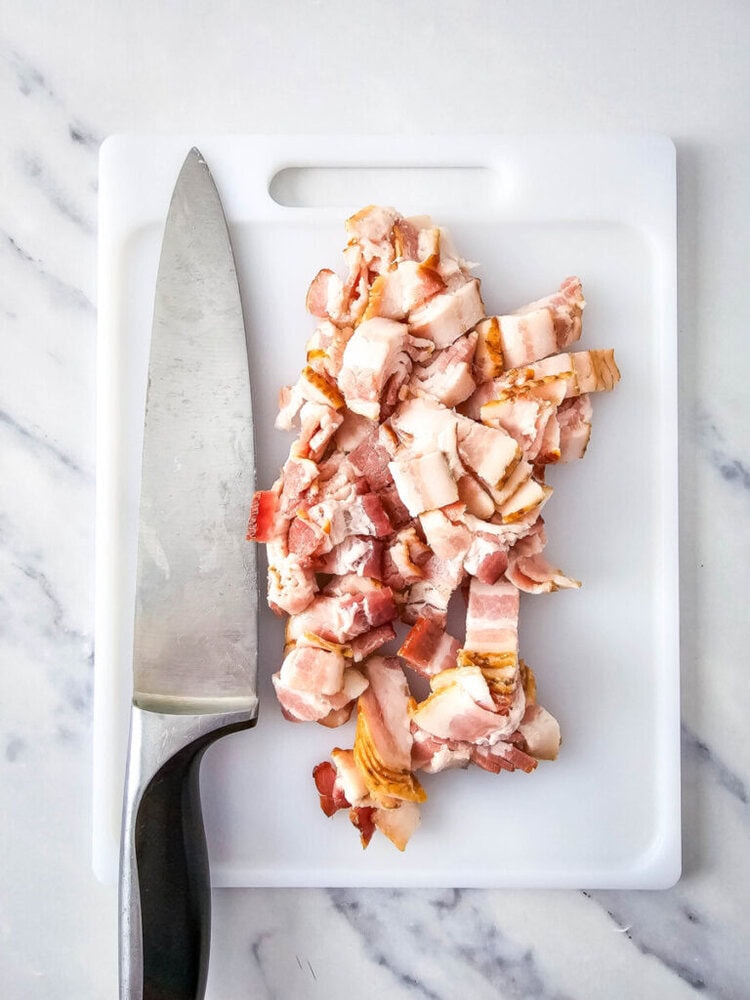Diced bacon on a white cutting board next to a large kitchen knife.