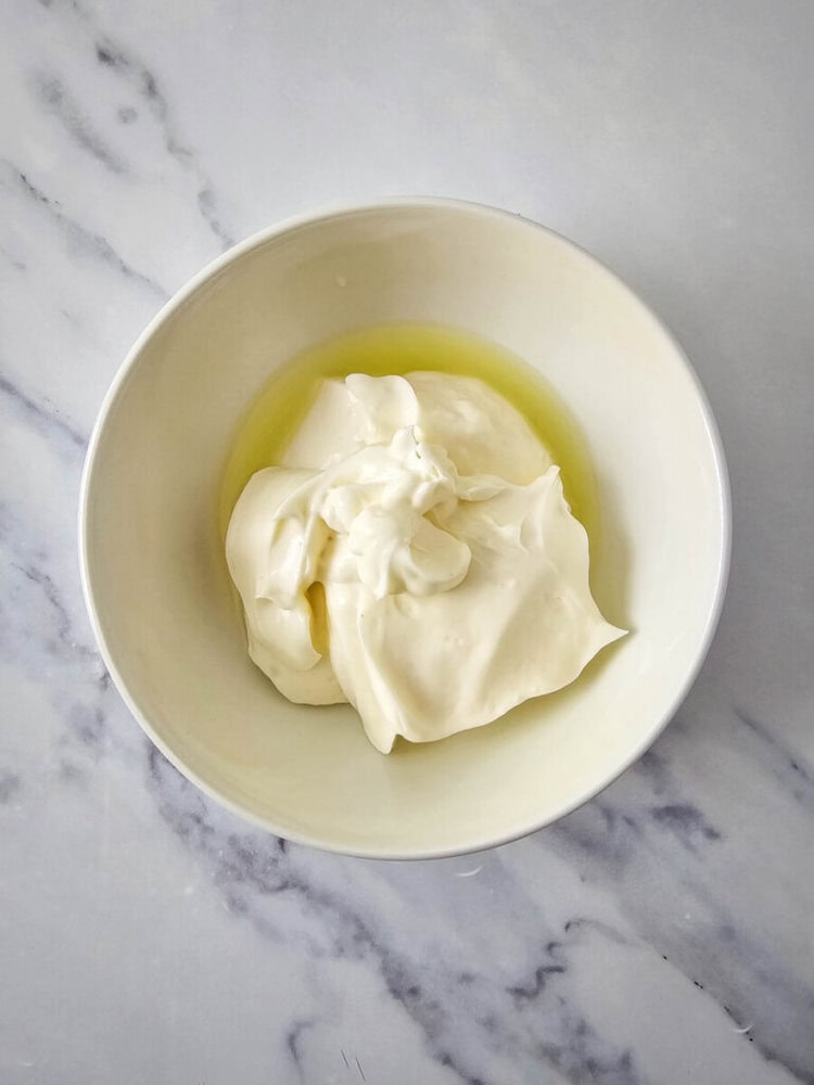 A white bowl containing a serving of mayonnaise on a marble countertop.