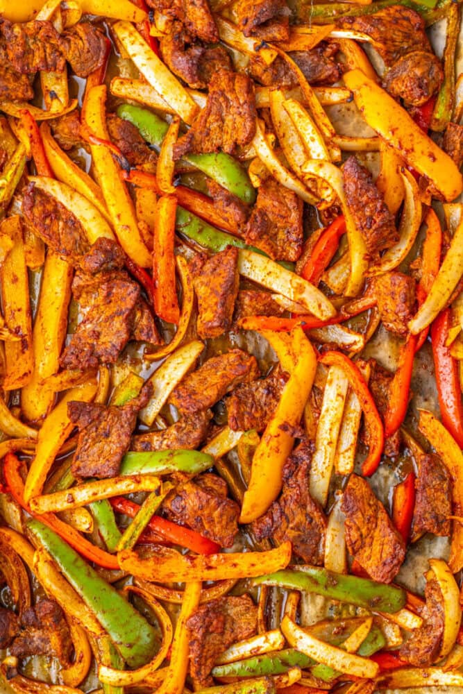 Colorful beef fajitas with sliced red, yellow, and green bell peppers and onions, seasoned and cooked on a sheet pan.