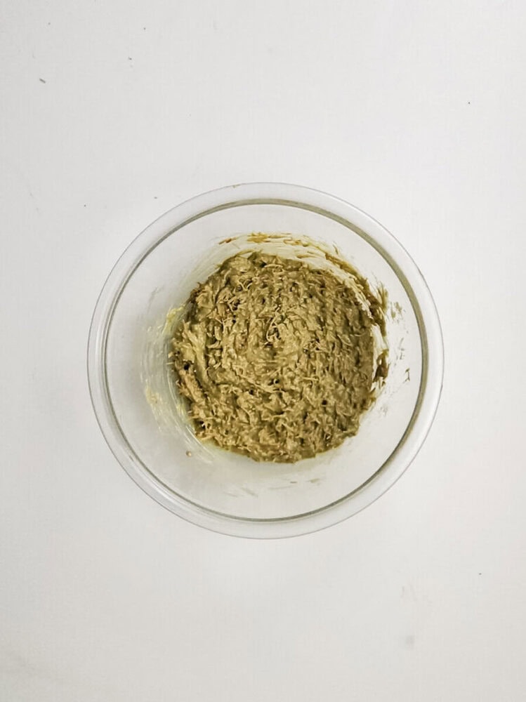 A clear glass bowl containing a mixture of shredded brownish-green material sits on a plain white surface.