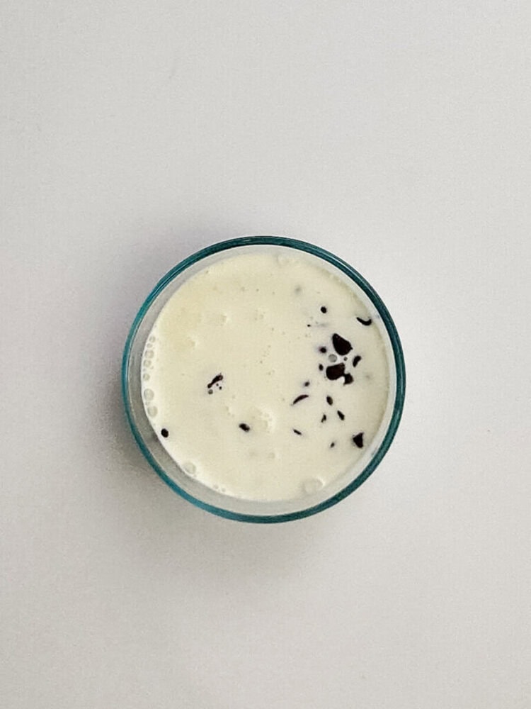 A small glass bowl filled with creamy white dessert or yogurt, topped with small chocolate chips, on a plain white surface.