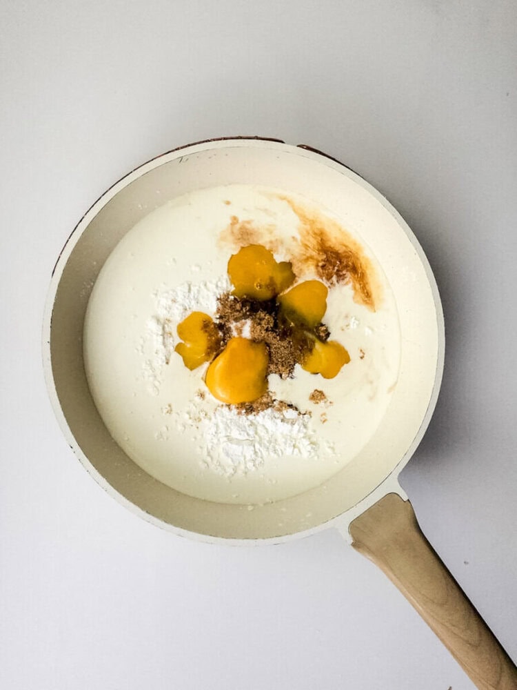 A white pan with cream, egg yolks, brown sugar, vanilla extract, and flour arranged separately, ready to be mixed.
