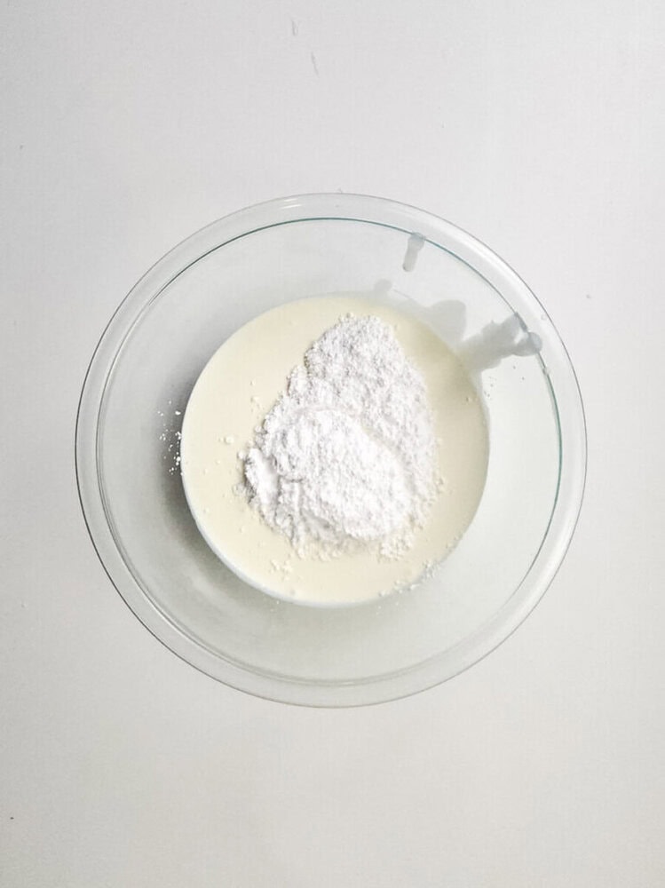 A glass bowl containing cream and powdered sugar on a white surface.