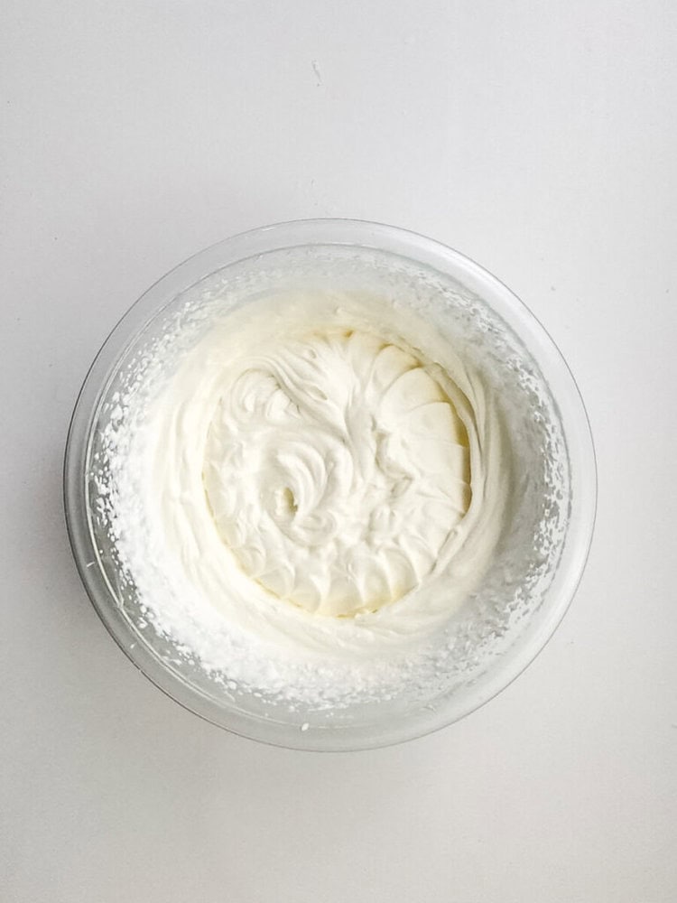 A glass bowl filled with whipped cream is placed on a white surface.