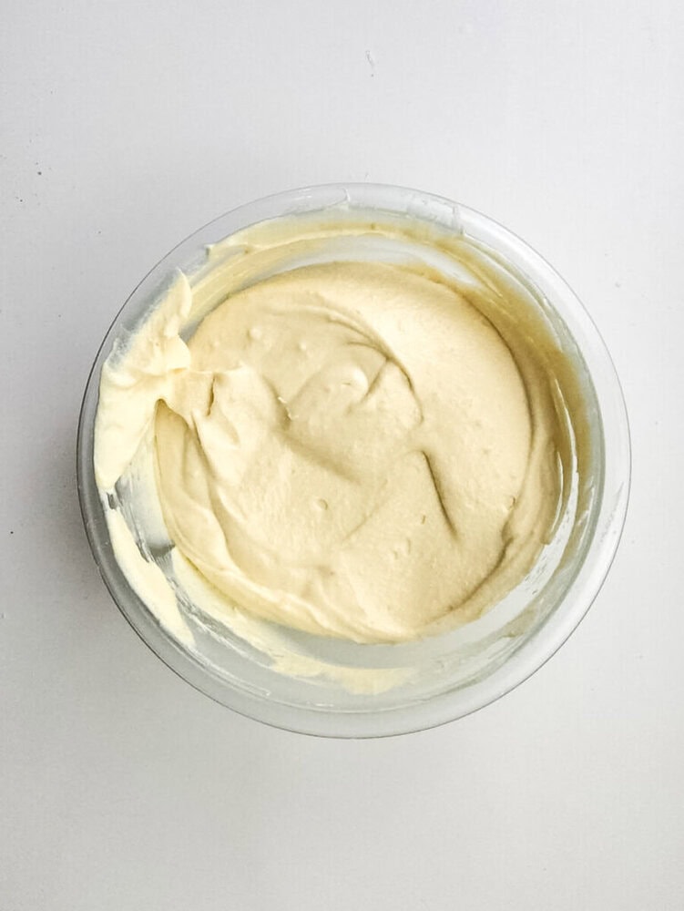 A clear glass bowl filled with smooth, creamy, pale yellow cake batter on a white surface.