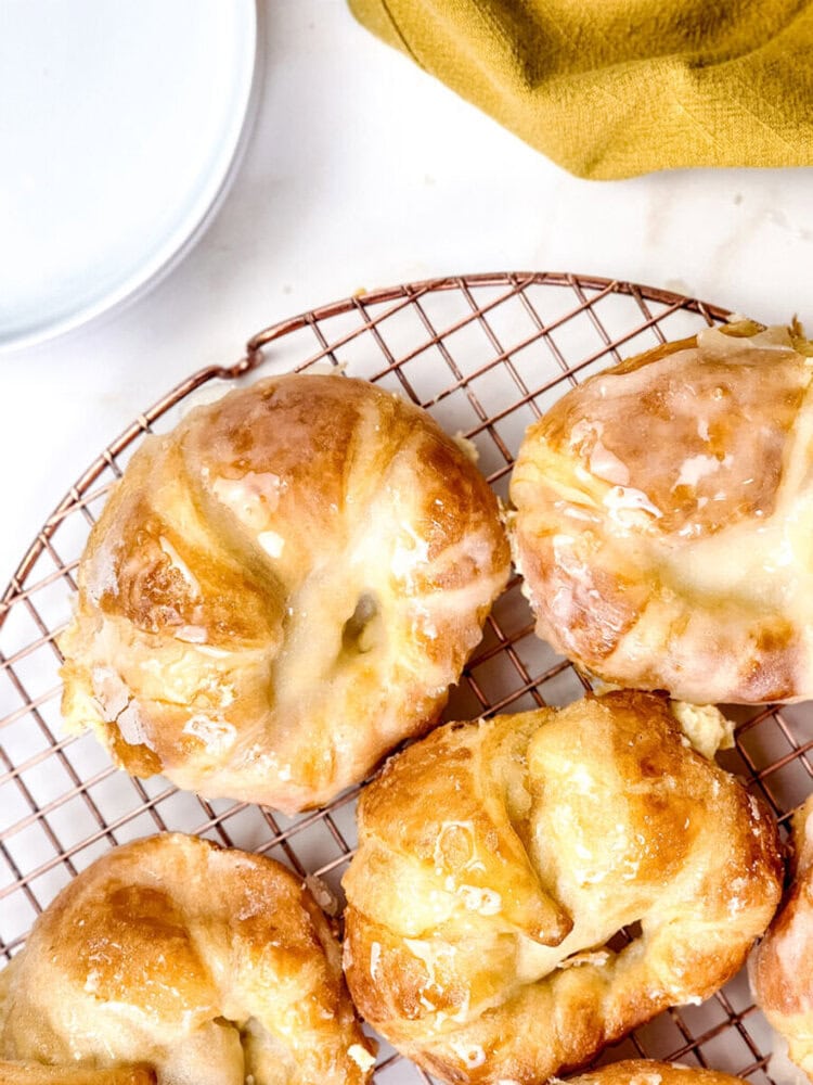 Glazed pastries cooling on a wire rack, with a white plate and a yellow cloth visible in the background.