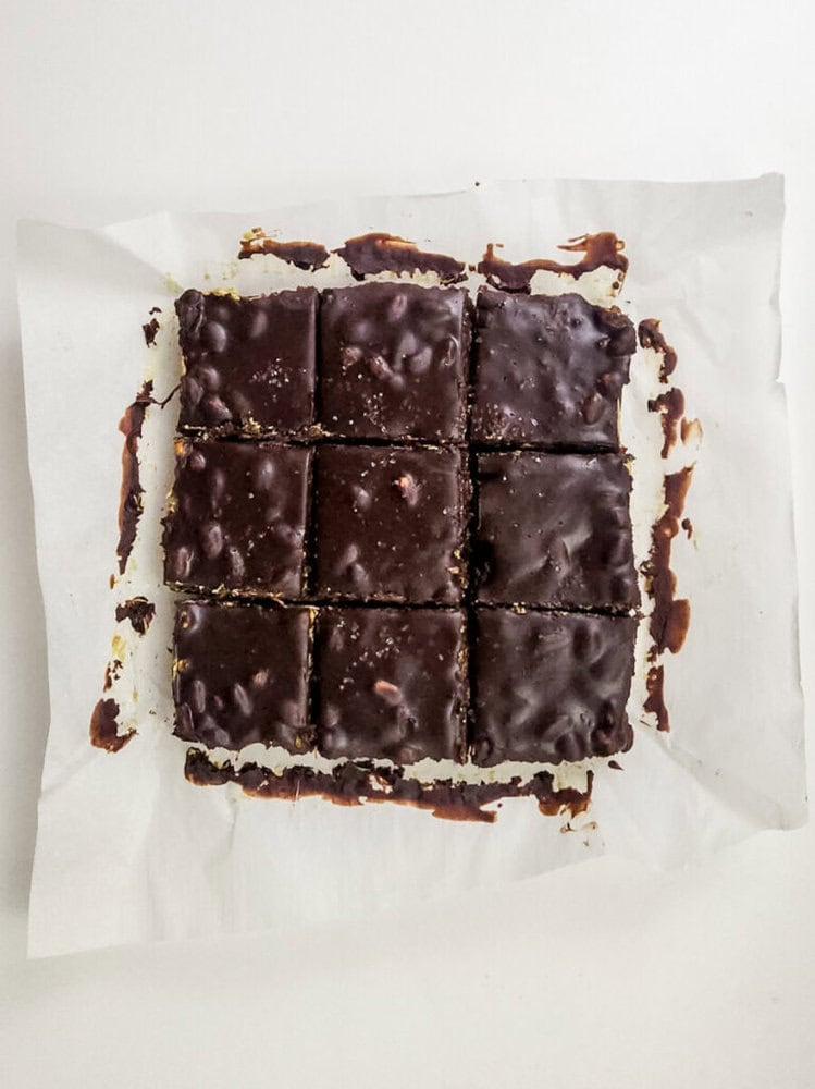 Nine chocolate-covered squares are arranged on parchment paper, each piece neatly cut and showing a glossy, textured chocolate coating.