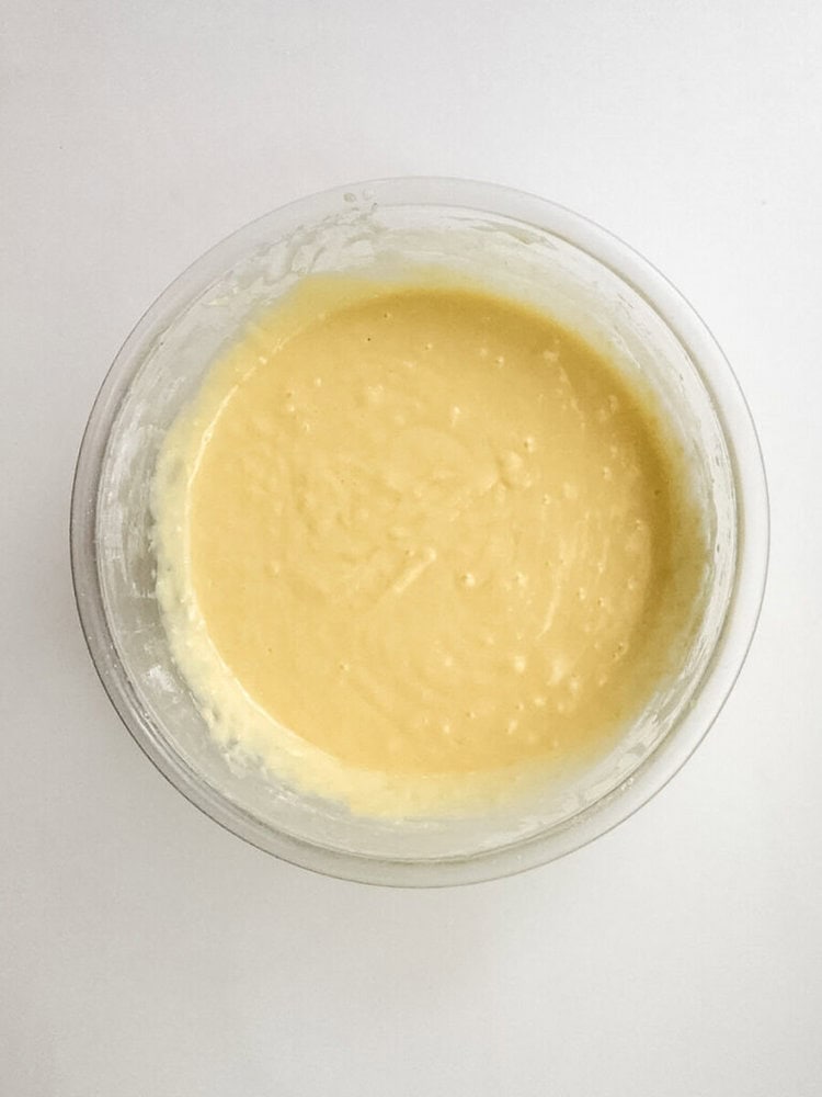 A clear glass bowl filled with smooth, yellow cake batter sits on a white surface.