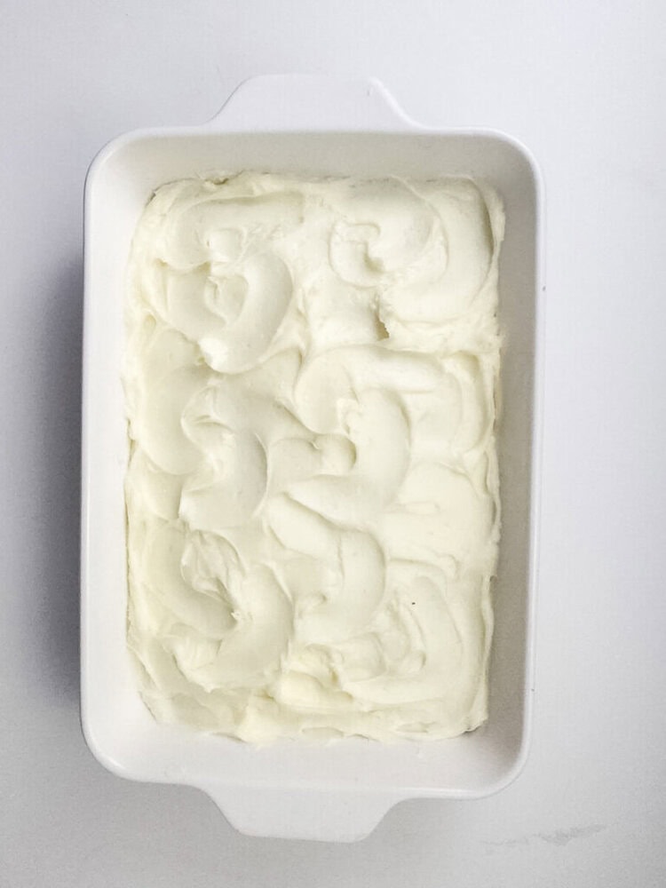 A rectangular white baking dish filled with a layer of smooth, swirled white frosting on top of a cake.