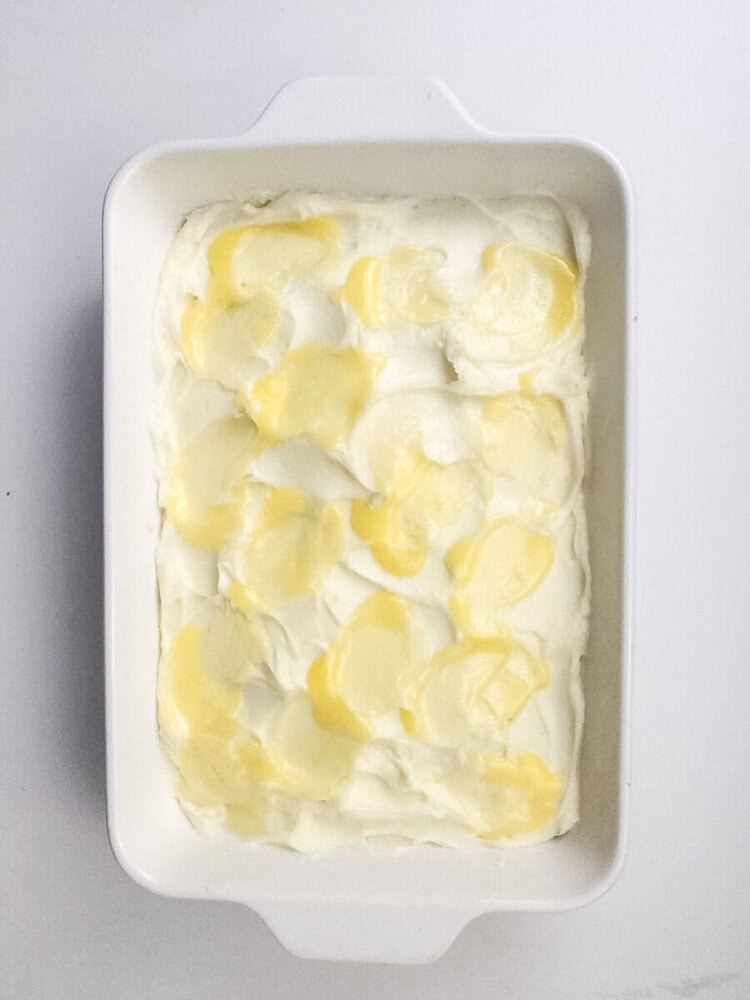 Rectangular white baking dish filled with a creamy white mixture, topped with uneven dollops of yellow butter.