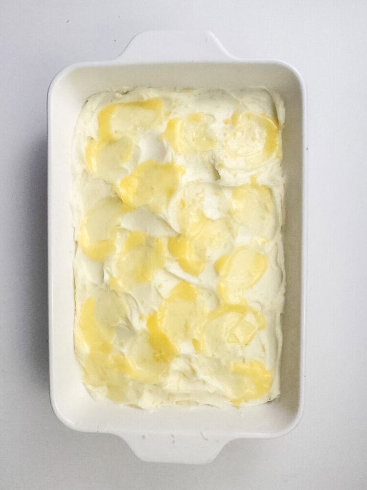 A white rectangular baking dish filled with sliced potatoes layered in a creamy white sauce, topped with melted butter.