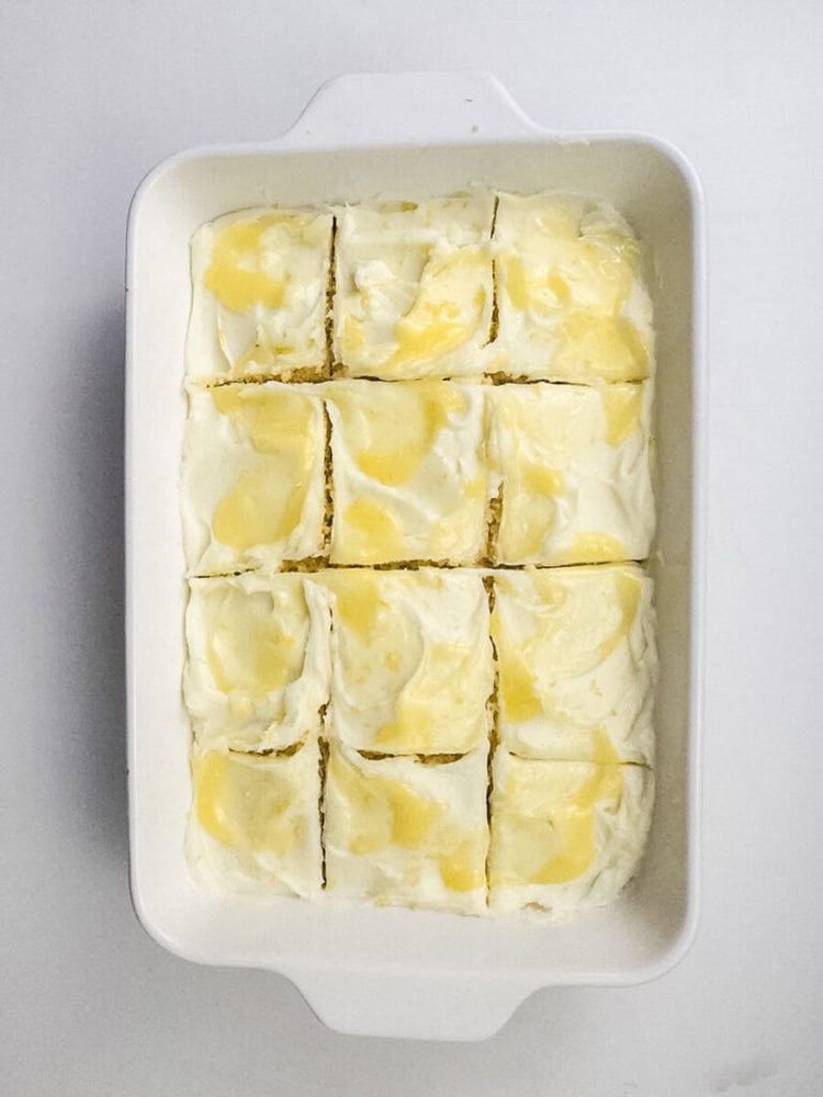 A white baking dish with nine square pieces of dessert topped with swirled yellow and white cream.