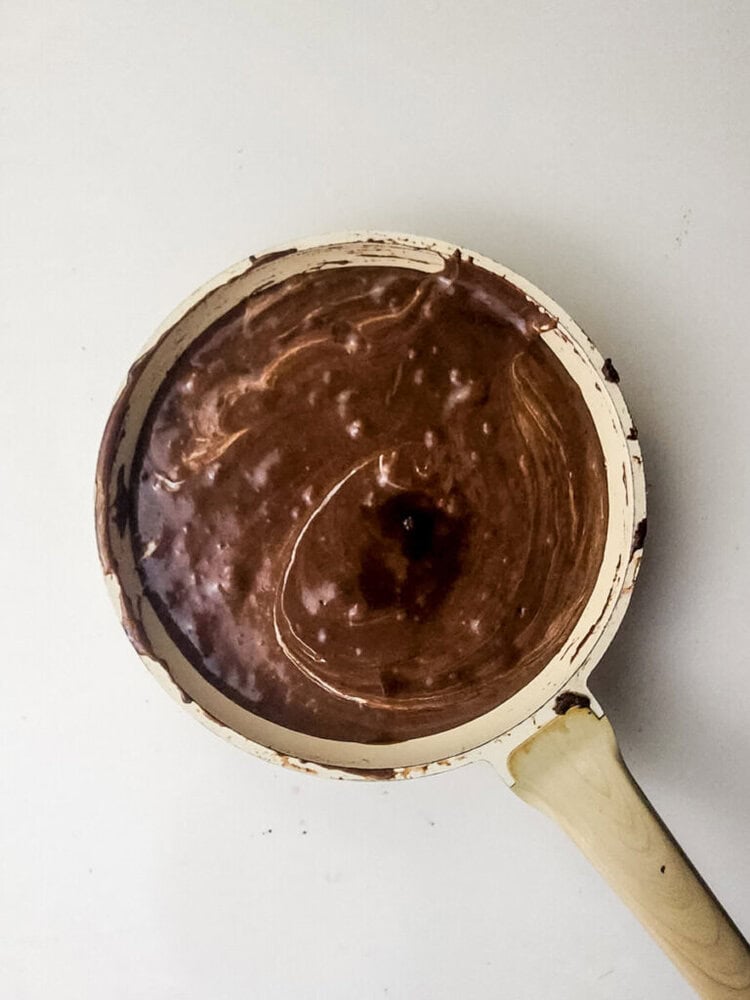 A pan with chocolate batter or sauce, showing swirled textures, rests on a white surface.