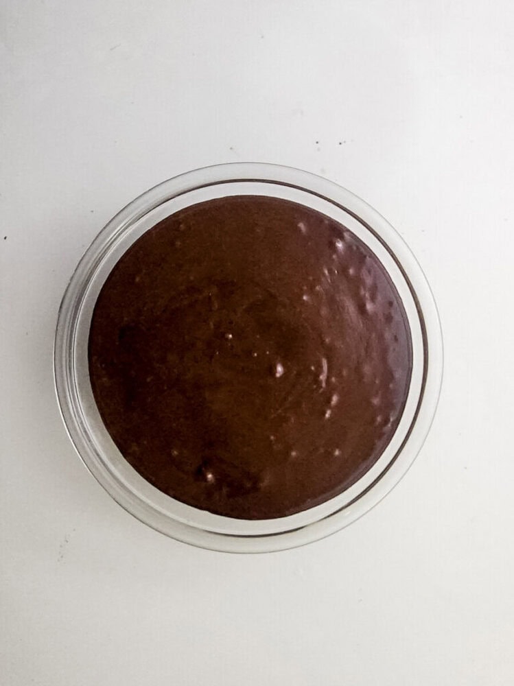 A glass bowl filled with chocolate cake batter sits on a white surface.