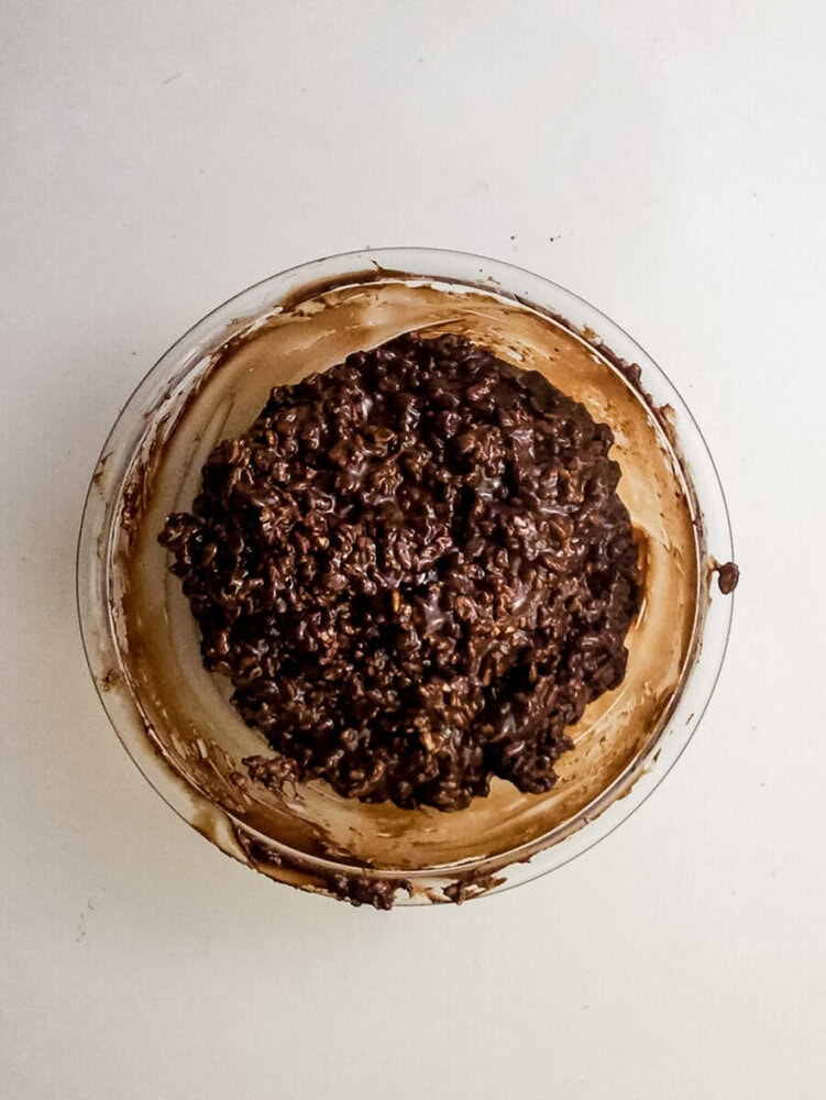 A glass bowl filled with a mixture of oats and chocolate sits on a white surface.