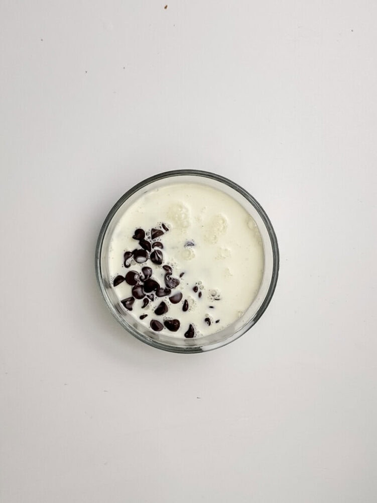 A glass bowl filled with white yogurt topped with chocolate chips, placed on a plain white surface.