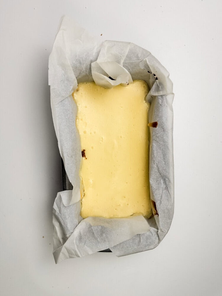 A rectangular cheesecake in a baking pan lined with parchment paper, viewed from above on a white surface.