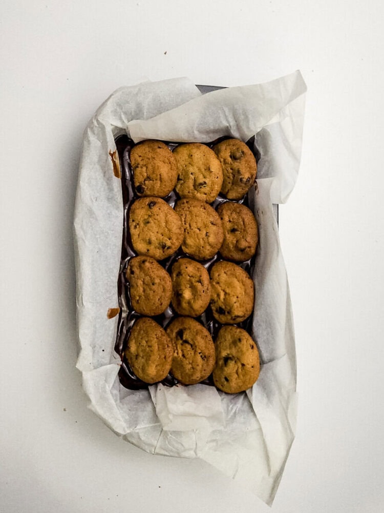 A rectangular baking pan lined with parchment paper holds a batch of chocolate chip cookies arranged in rows.
