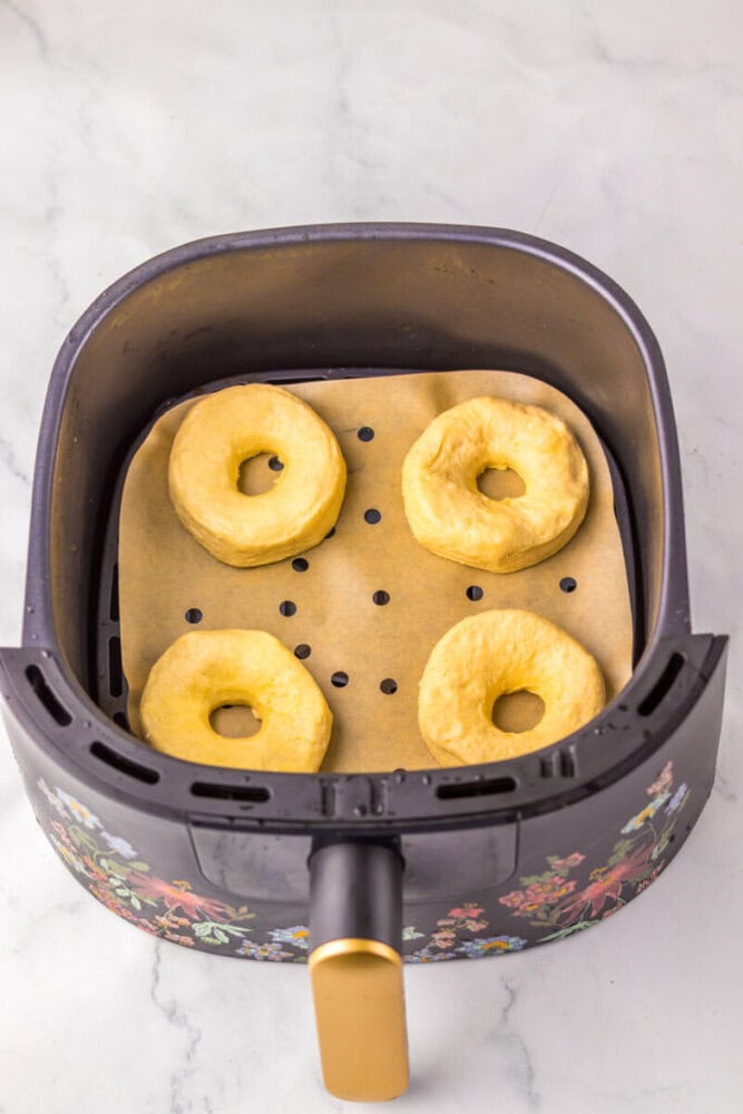Four unbaked biscuit dough rings are placed on a parchment-lined tray inside an air fryer basket, ready to be cooked.