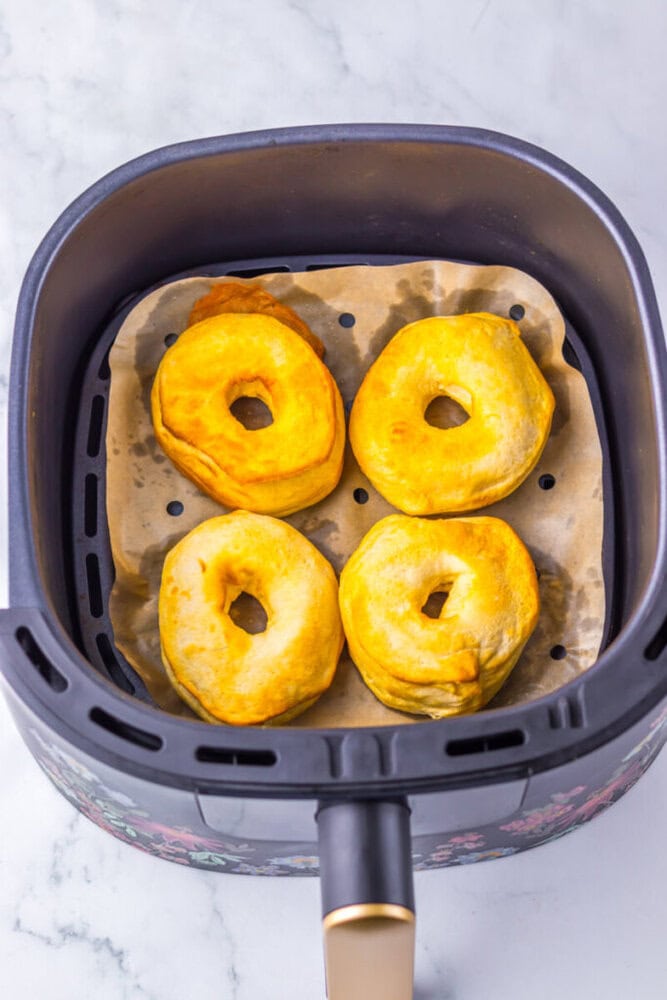 Four golden-brown biscuit donuts on parchment paper inside an air fryer basket.